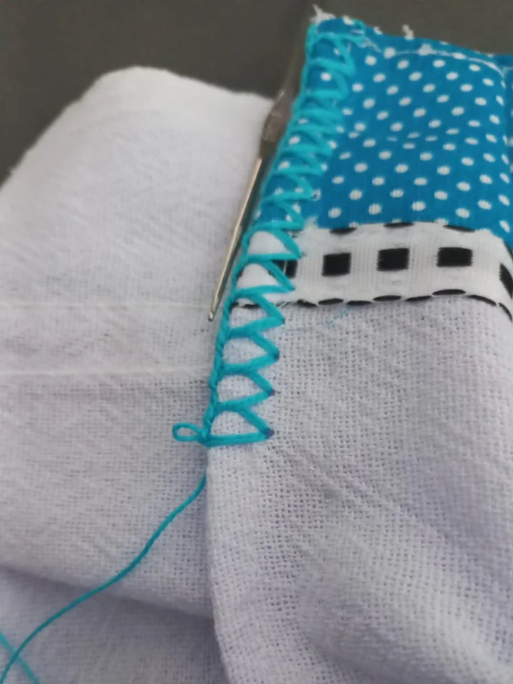 Barrado em crochê sendo feito à mão, com agulha e linha turquesa, contornando a borda de um pano de prato em patchwork